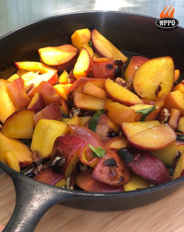 Skillet with roasted fruit and vegetables cooking inside a wood-fired oven