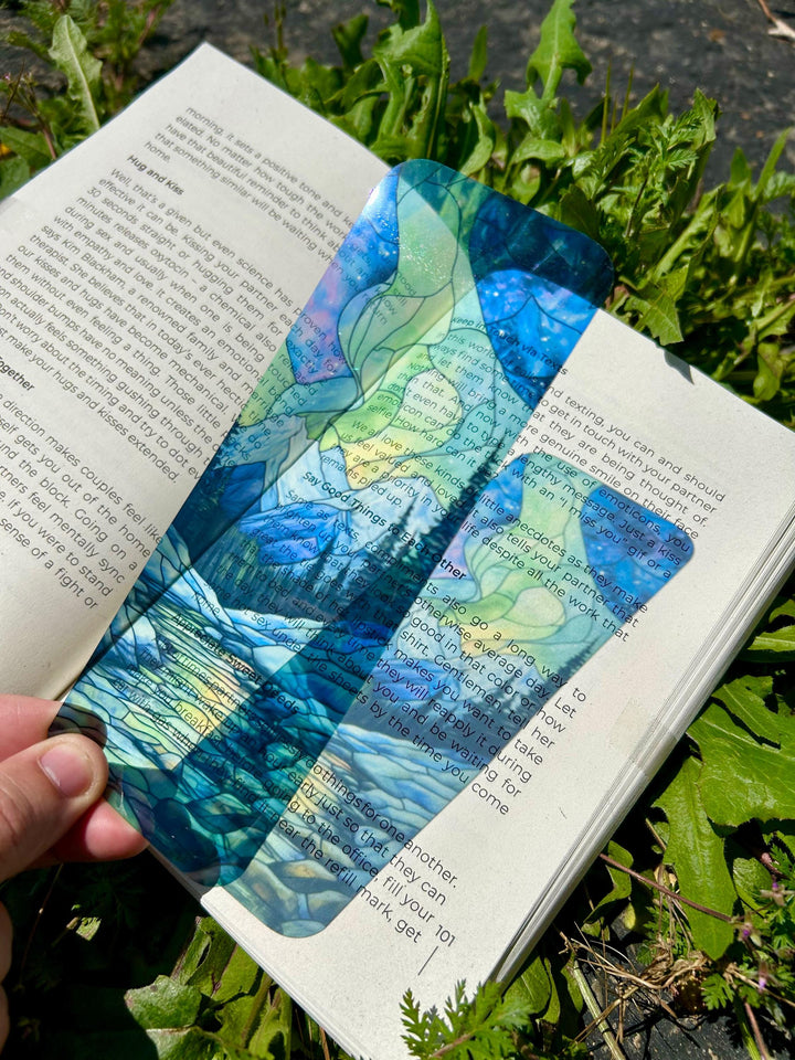 Handmade aurora-stained glass bookmark, blue and green wave pattern, on open book