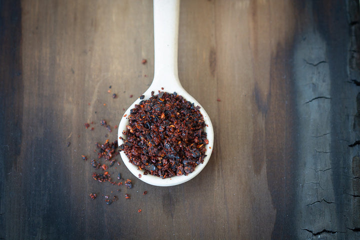 Chili-lime spice blend in white spoon, dark red-brown granules