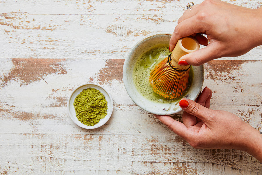 Culinary matcha powder being whisked with a brush in a ceramic bowl