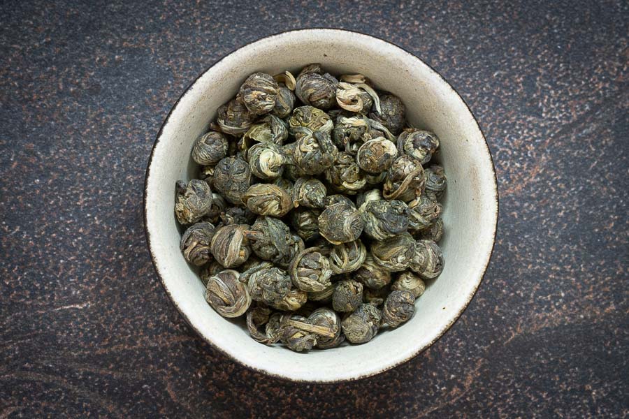 Rolled jasmine tea pearls in a white bowl, green and speckled with buds
