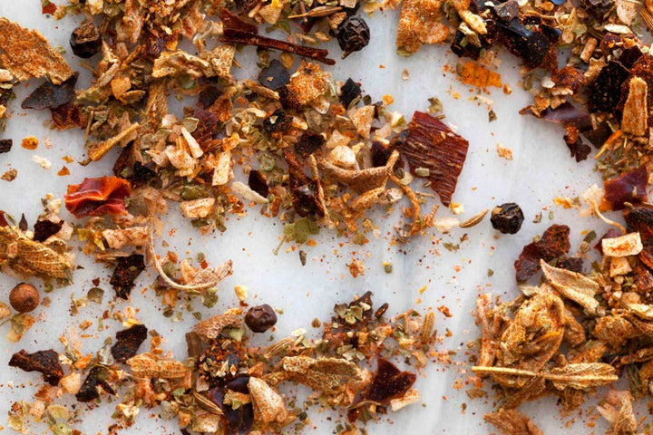 BBQ rub seasoning flakes and herbs, scattered on a white surface