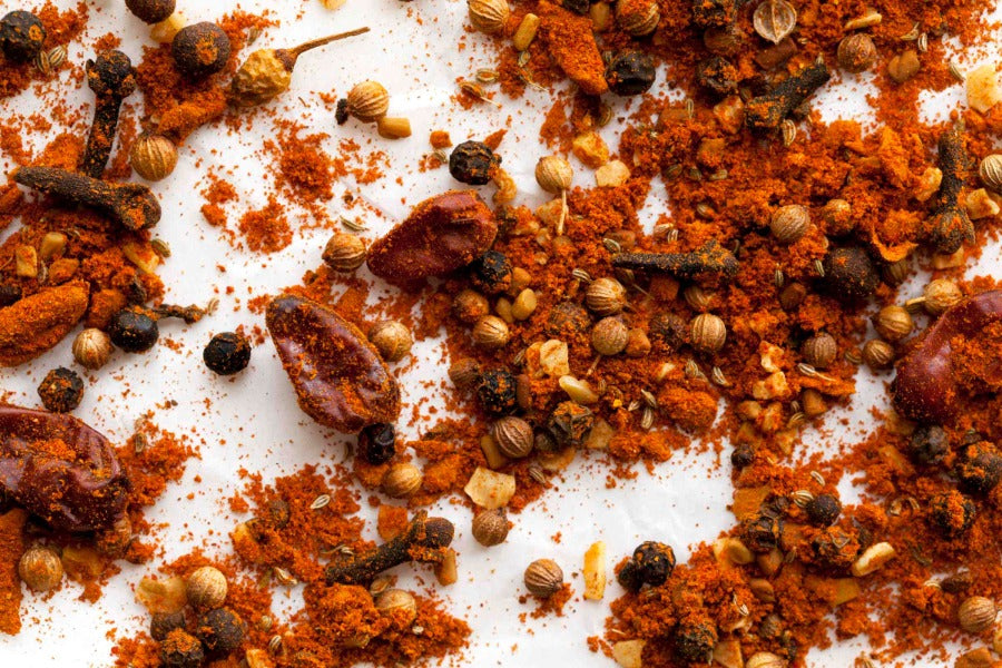 Ground spice blend with orange-brown crumbs and seeds on white surface