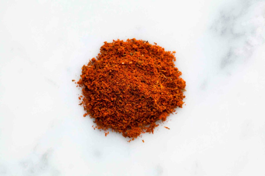 Mound of Cajun seasoning spice blend, finely ground red-orange mix on white surface
