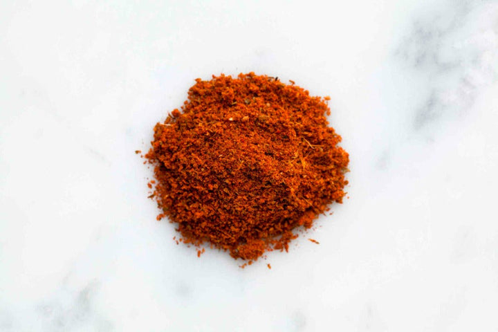 Mound of Cajun seasoning spice blend, finely ground red-orange mix on white surface