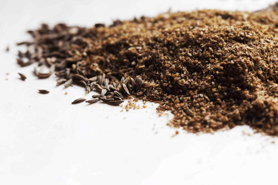 Ground caraway seed, fine dark brown powder piled on a white surface.