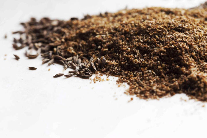 Ground caraway seed, fine dark brown powder piled on a white surface.