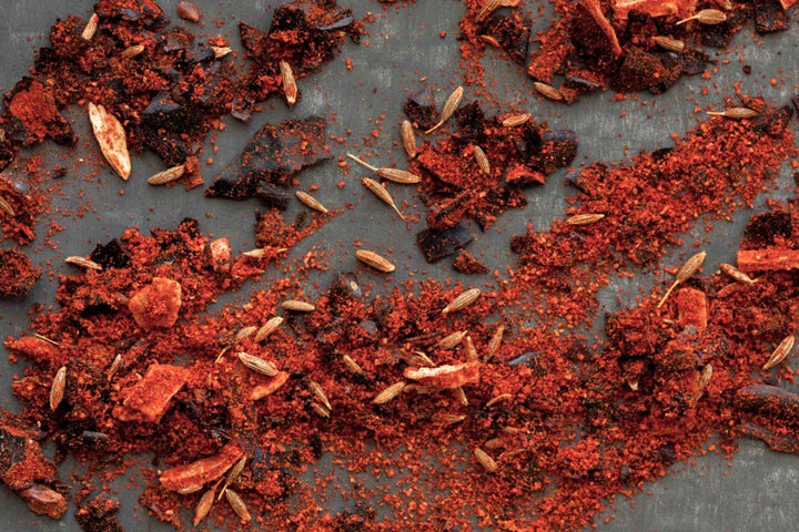 Chipotle chili powder, red-brown spice flakes and small seeds scattered on a surface