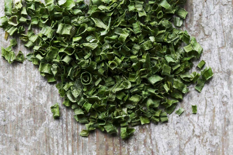 Chopped chives: small green herb pieces scattered on a wooden surface