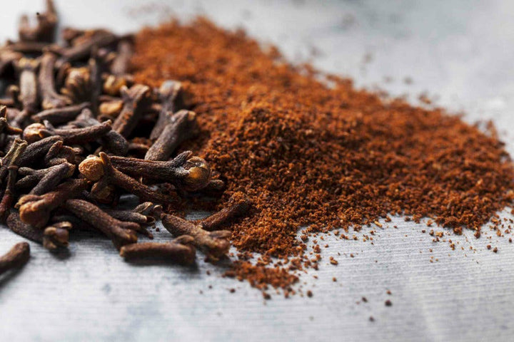 Ground cloves spice powder heap with scattered clove pieces