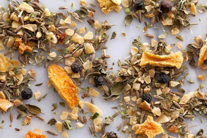Whole spice mix with leaves, berries, and crushed pepper on a flat surface
