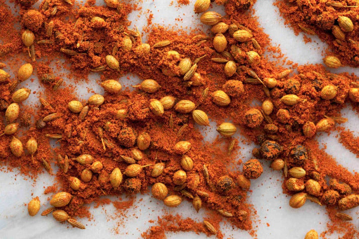 South African curry spice blend with scattered seeds and ground powder on white surface