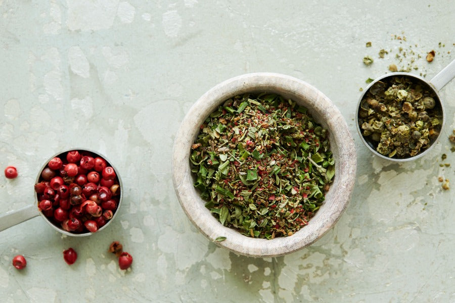 Herbal seasoning mix in a bowl, with small bowls of chopped spices beside it.