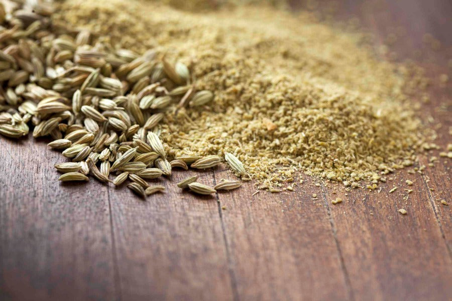 Ground fennel seed powder and loose granules on a wooden surface