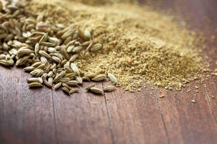 Ground fennel seed powder and loose granules on a wooden surface