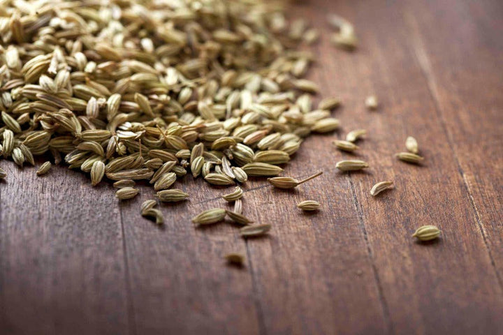Whole fennel seeds scattered on a wooden surface