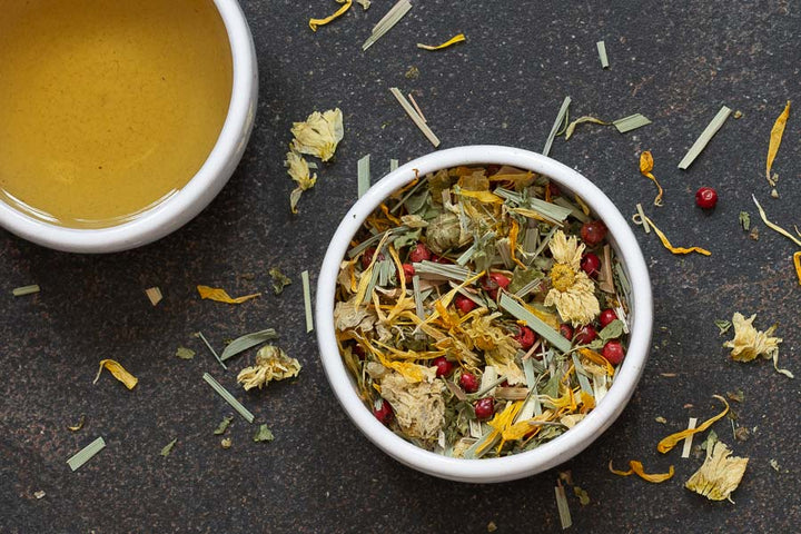 Loose herbal tea leaves in a small white bowl, with scattered dried ingredients
