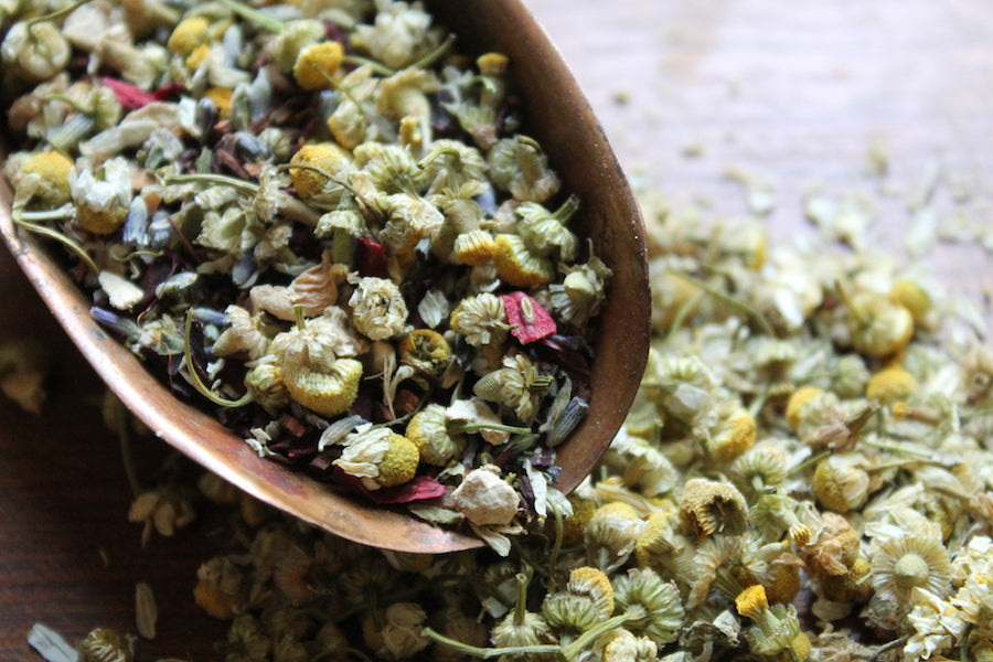 Dried floral tea mix in wooden spoon, with small blossoms and herbs