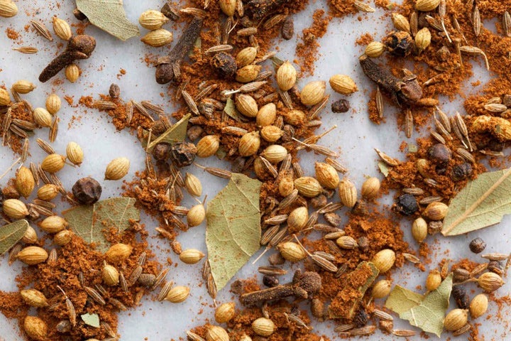 Indian garam masala spice blend with whole spices and scattered bay leaves