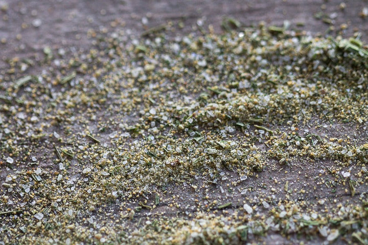 Garlic salt seasoning blend with green herbs on a flat surface
