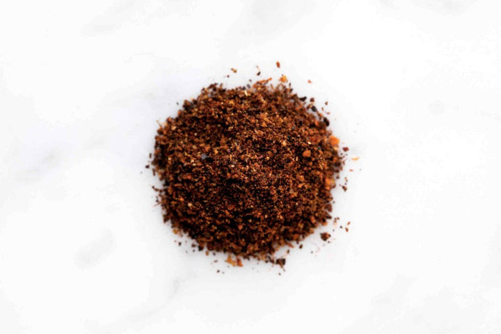 Finely ground brown-red harissa spice blend pile on light surface