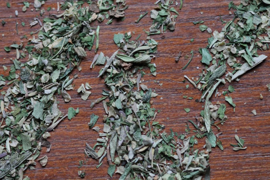 Dried green herbes de Provence herb flakes, scattered on wooden surface