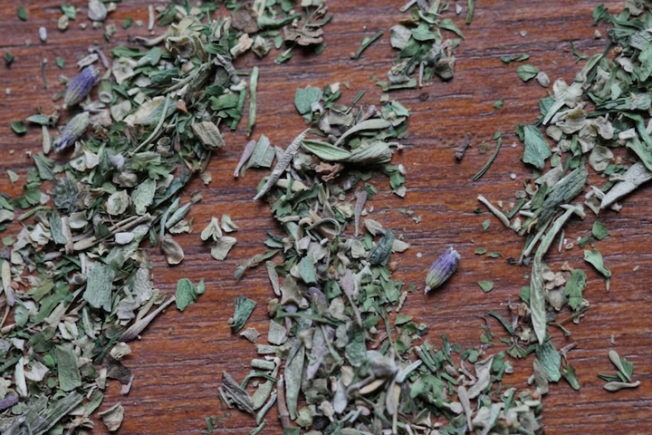 Dried Herbes de Provence herb flakes spread on a wooden surface.