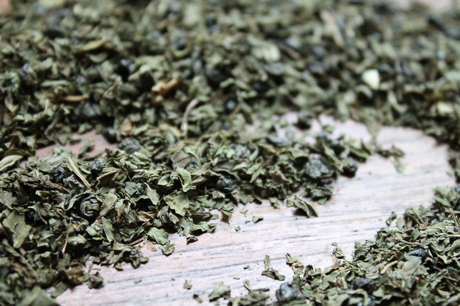 Loose green mint tea leaves spread on a light wood surface.