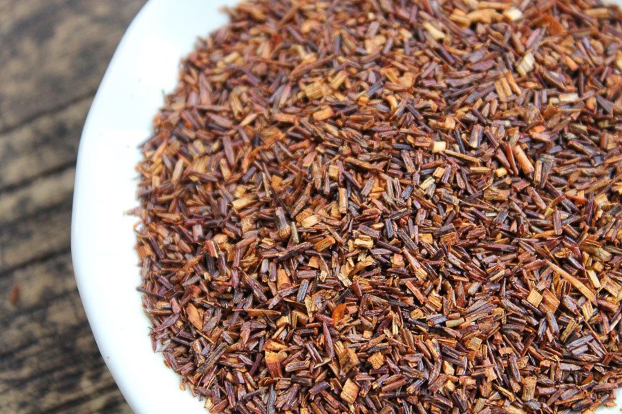 Cut and sifted rooibos tea leaves, loose dark reddish-brown in a white dish.