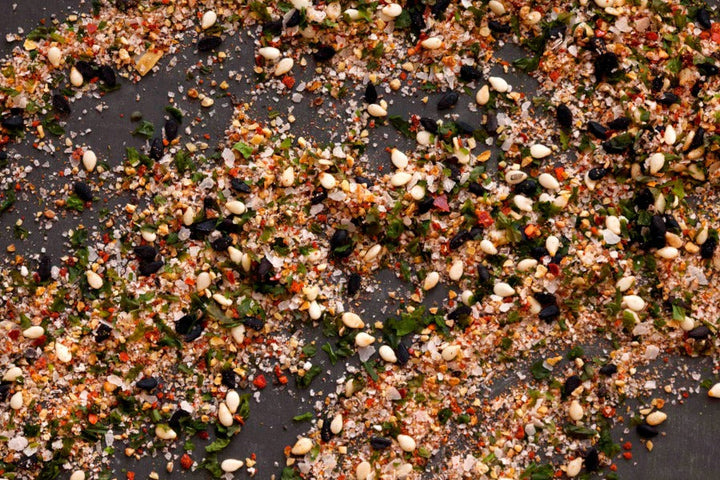 Seasoned salt spice blend with herbs and flakes scattered on a dark surface