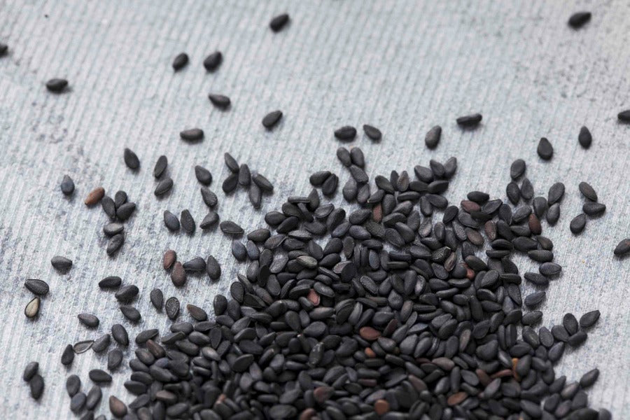 Black sesame seeds, whole grains scattered on a surface.