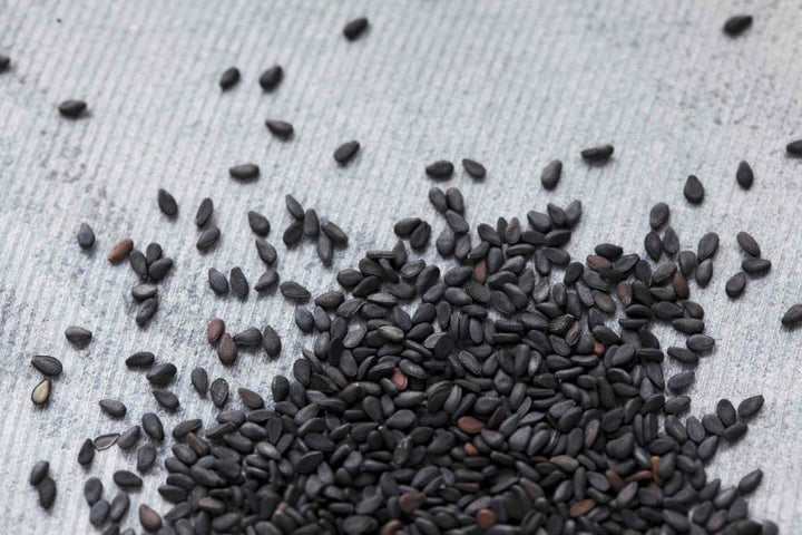 Black sesame seeds, whole grains scattered on a surface.