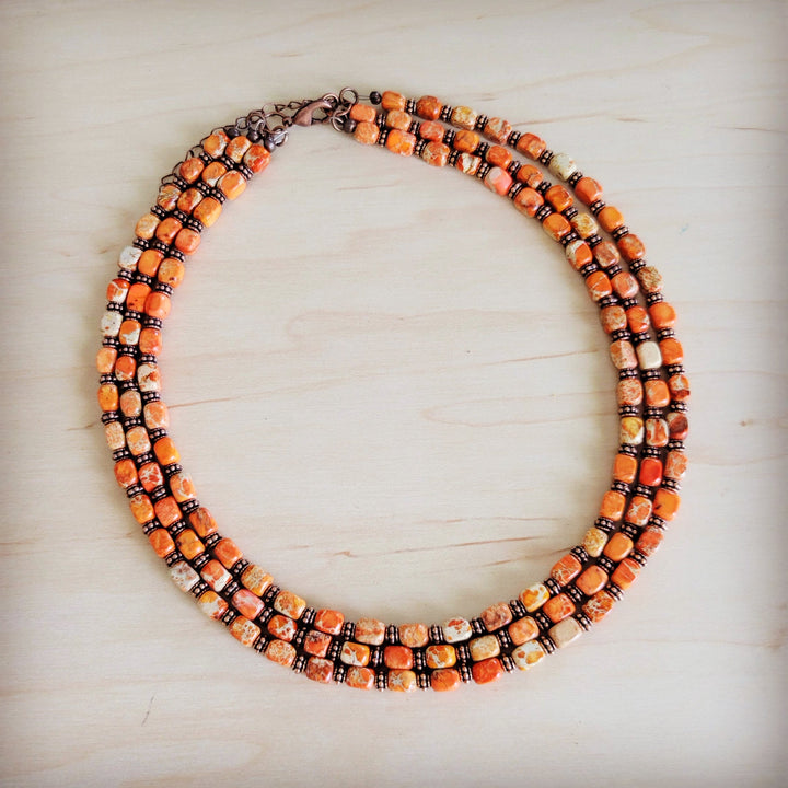 Layered triple strand beaded necklace in orange, cream, and bronze with curved clasp