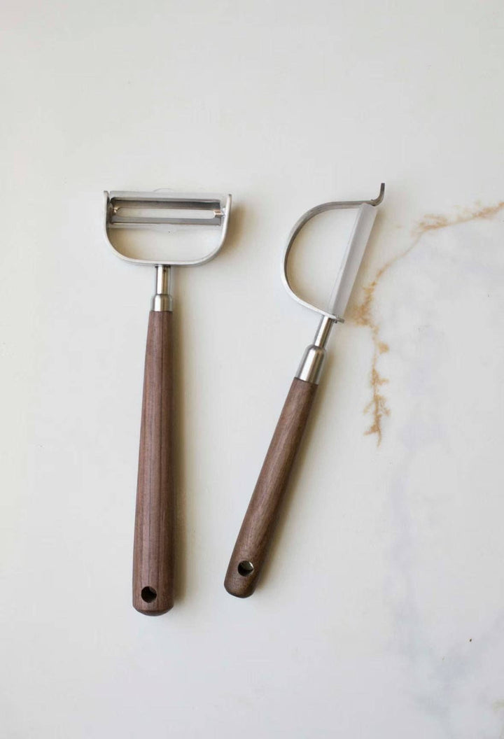 Stainless steel vegetable peelers with brown wooden handles, curved blade and hanging loop