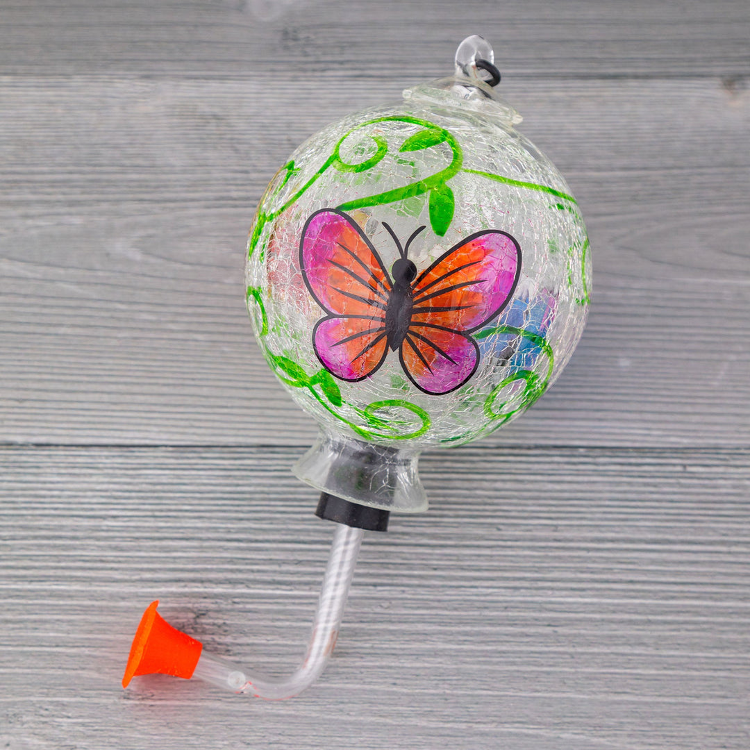 Hanging glass hummingbird feeder ornament with green vines and a purple-orange butterfly