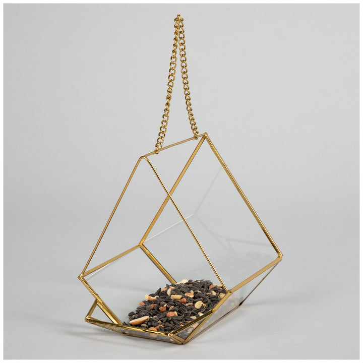 Hanging glass bird feeder with gold metal frame and chain, filled with birdseed