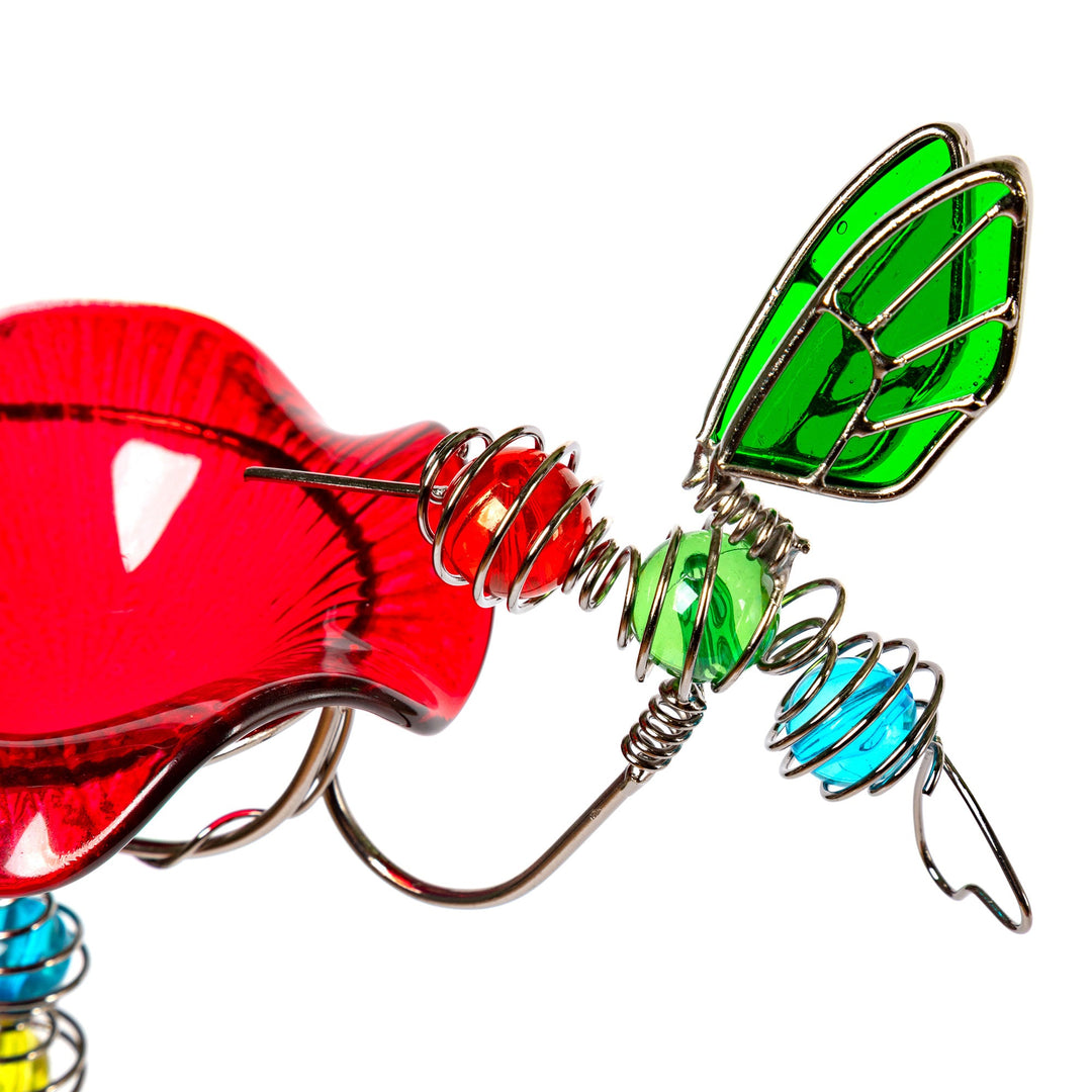 Stained glass hummingbird feeder close-up with red glass body, green wings, and blue accents.