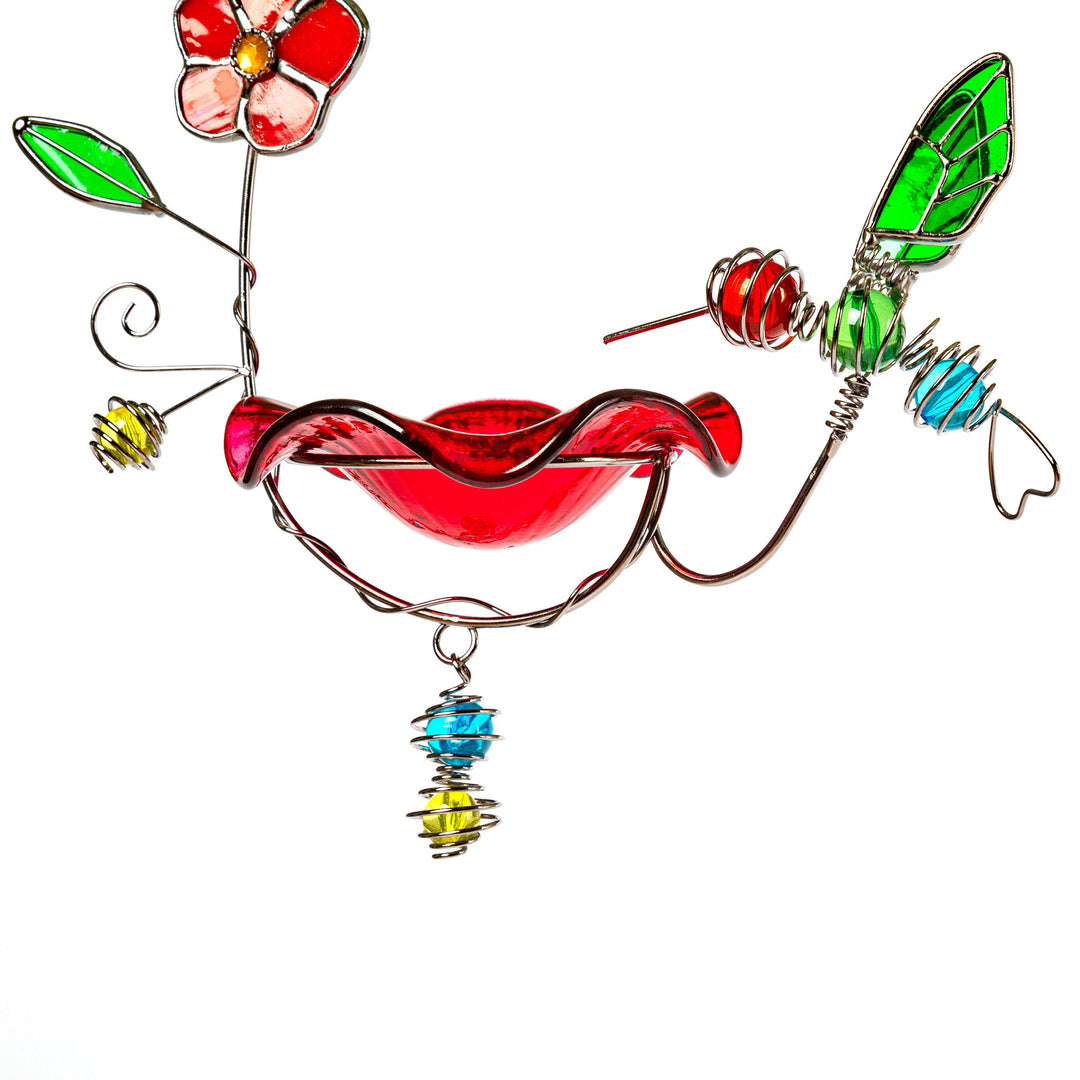 Stained glass hummingbird feeder with red glass body, green wings, and dangling bell charm.