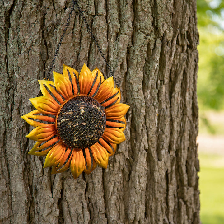 Hanging sunflower mesh bird feeder on a tree, golden petals around dark wire mesh core