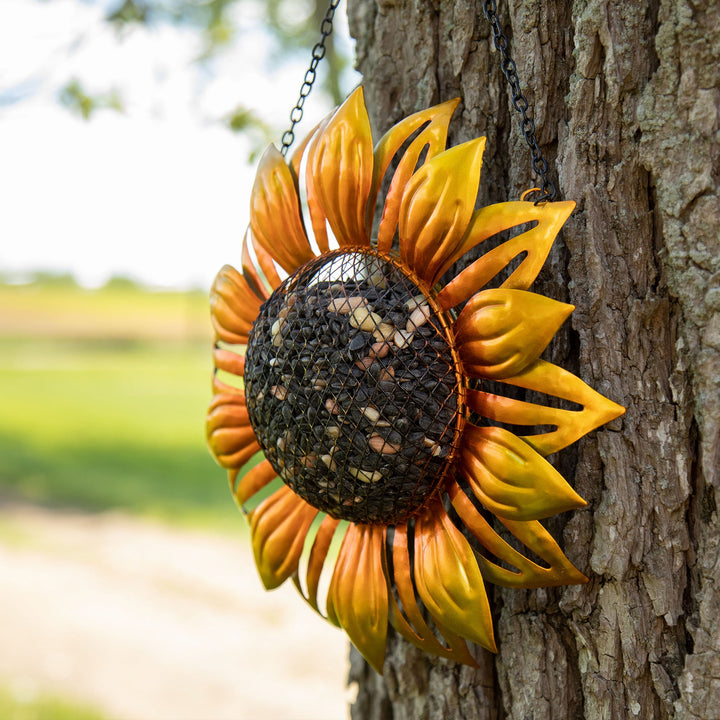 Hanging sunflower bird feeder on a tree, golden petals around dark mesh seed core