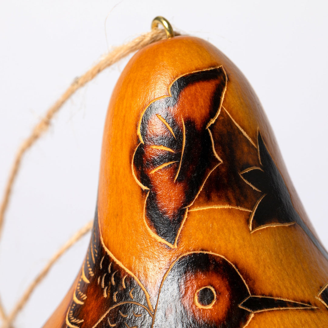 Close-up gourd birdhouse top, orange with black leaf pattern and small vine detail