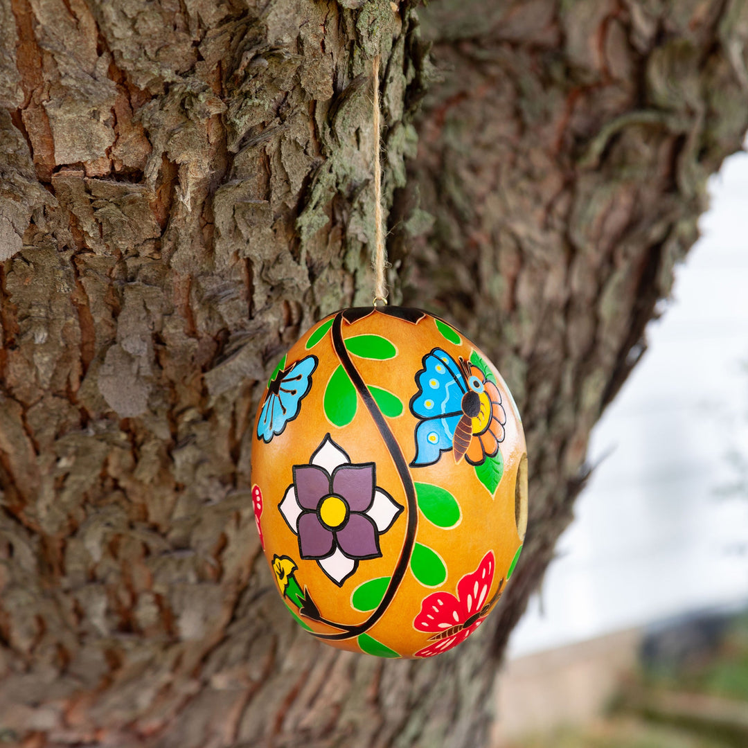 Hand-painted gourd birdhouse hanging on tree branch with colorful flower and leaf patterns