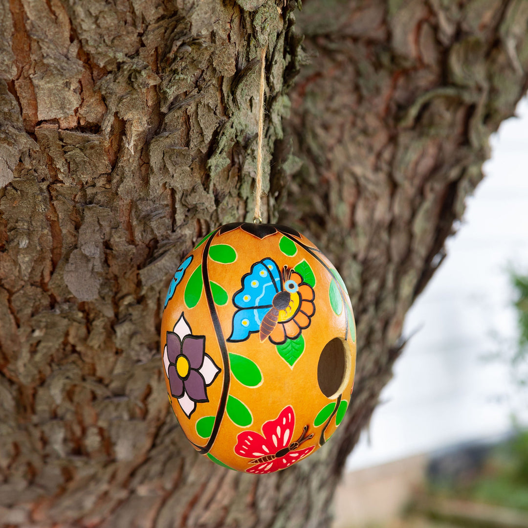Hand-painted gourd birdhouse hanging on a tree branch with butterfly and flower art