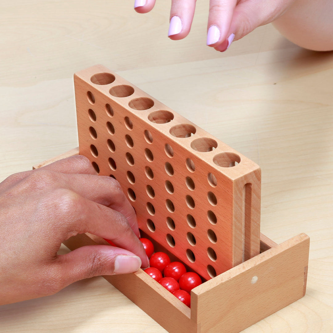 Hands loading red pegs into wooden peg board game trough and holes