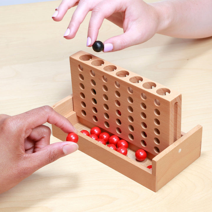 Hands inserting a black peg and moving red pegs in a wooden peg board game