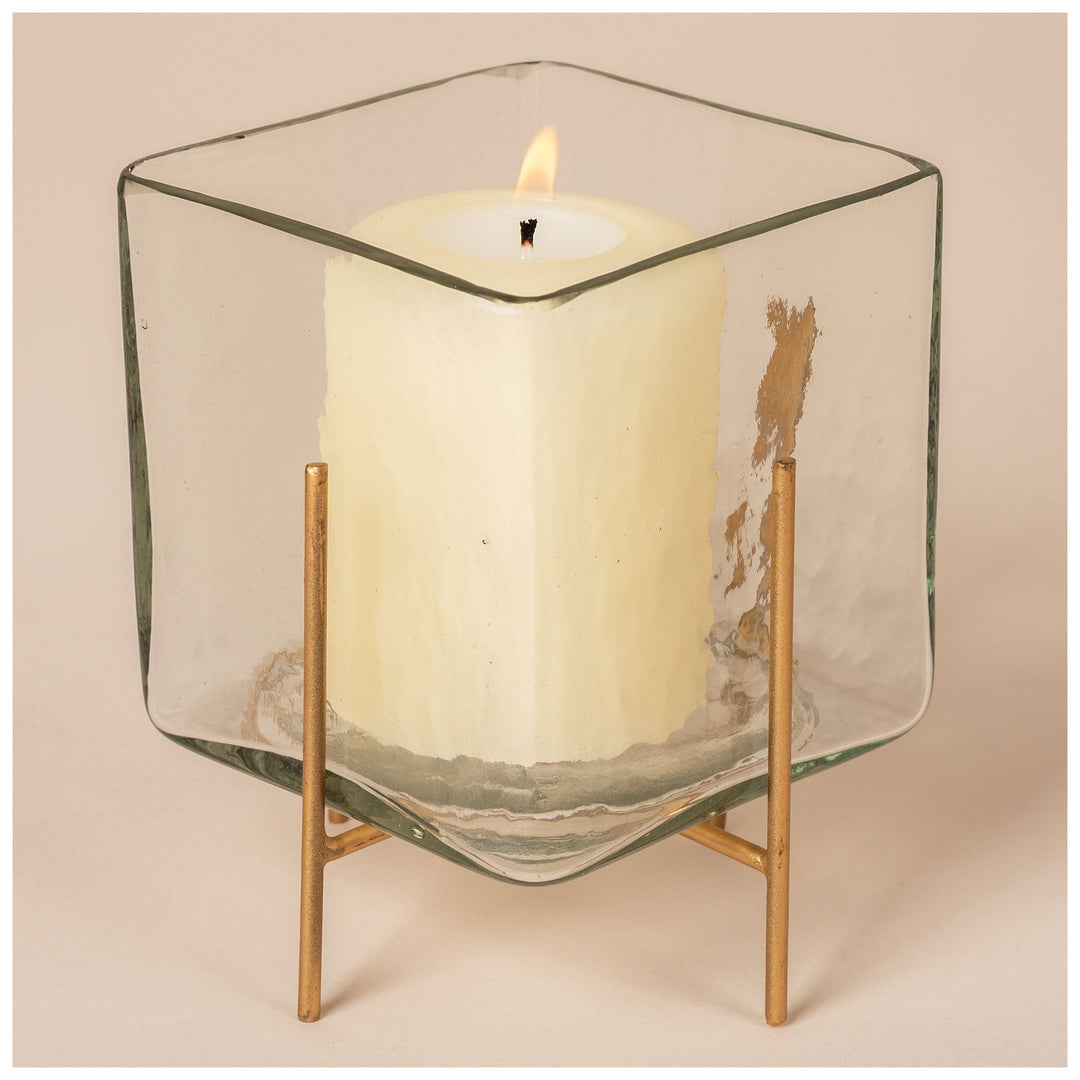 Square glass tea light holder with burning candle, clear glass walls and brass legs