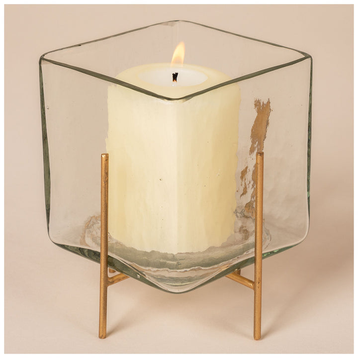 Square glass tea light holder with burning candle, clear glass walls and brass legs