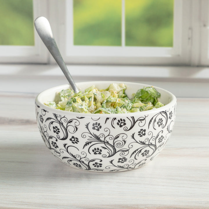 Ceramic bowl with black paw-and-floral swirl pattern, filled with salad and spoon