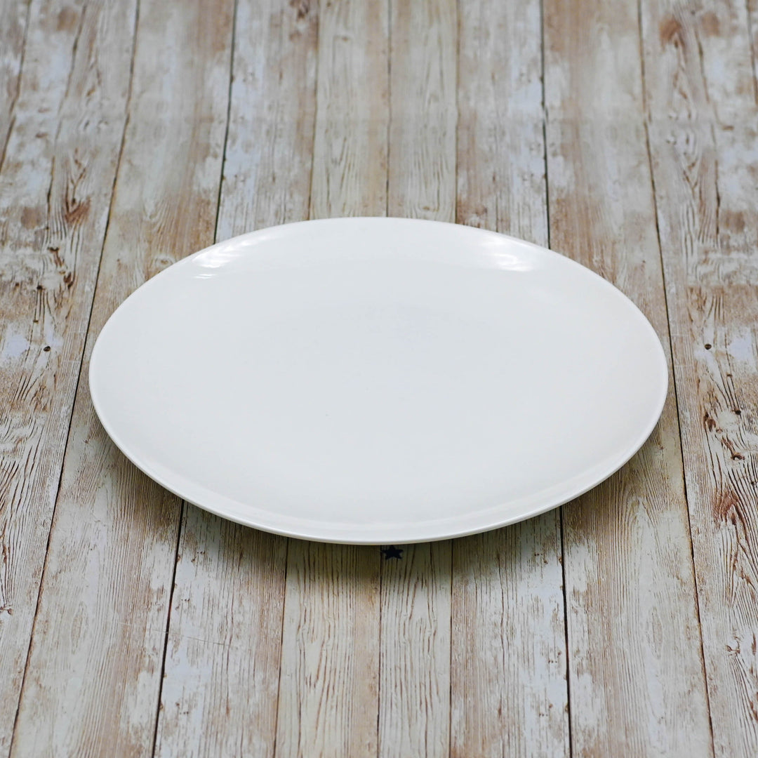 White round dinner plate with smooth edge, set on light wood surface.