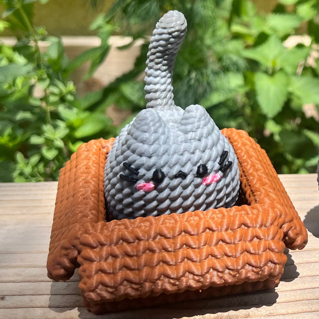 Knitted cat plush with orange pouch, gray textured body and pink nose whiskers